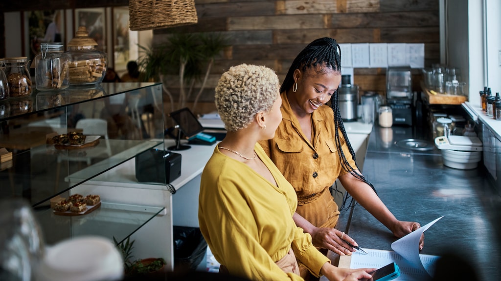 Small business owners talking and discussing the performance of their coffee shop. Black female entrepreneurs in a partnership collaborating and planning growth together inside their cafe or shop