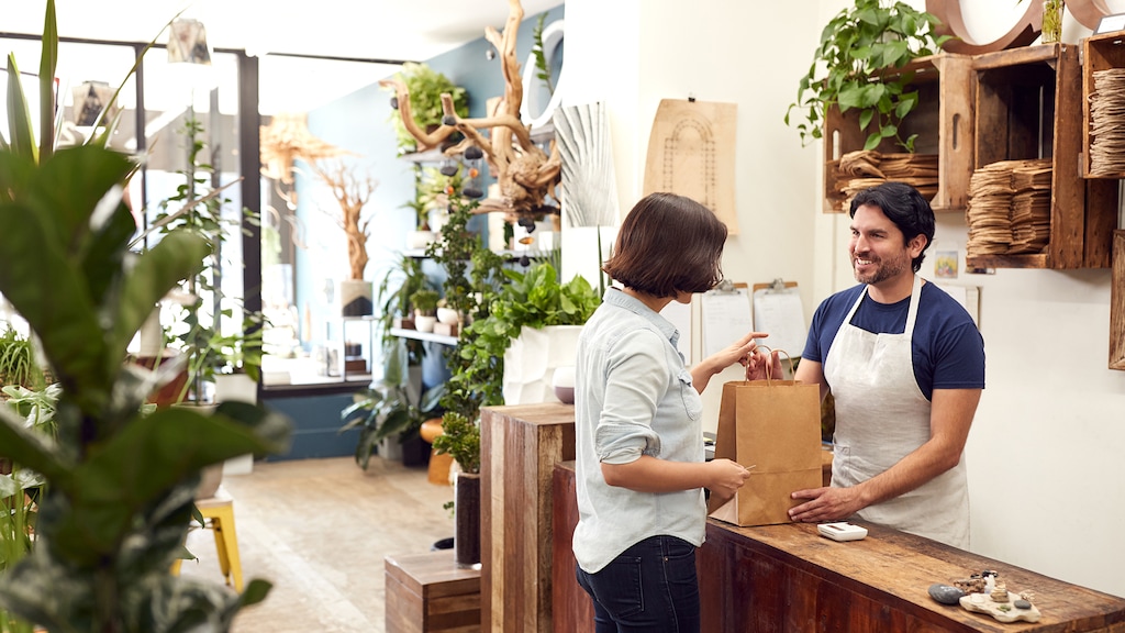 Male Sales Assistant In Florists Shop Serving Female Customer At Sales Desk